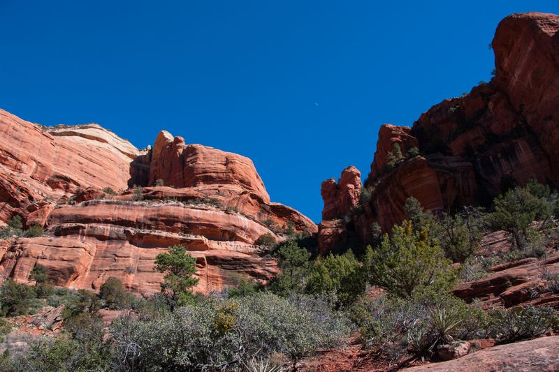 Red sandstone cliffs and spires under a deep blue sky above scrub and juniper on Boynton Canyon Trail, Sedona