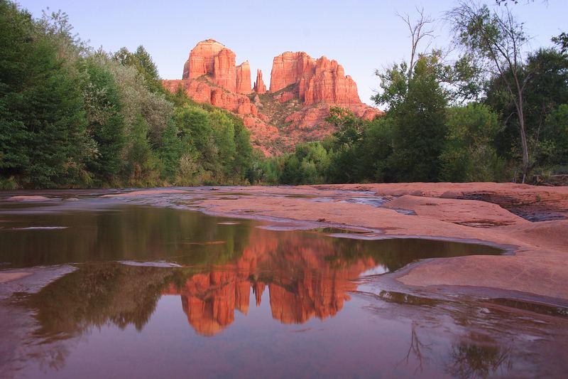 Cathedral Rock's red sandstone spires reflected in still water on the creek-side slickrock at Red Rock Crossing, Sedona, after sunset
