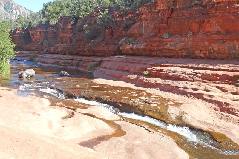 Oak Creek running down a narrow chute in the smooth red sandstone creek bed at Slide Rock State Park, below red cliffs